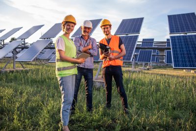 Charismatic group of investors and ecological engineer pretty woman all with safety helmets analysing the plan of work at photovoltaic solar panels farm.
